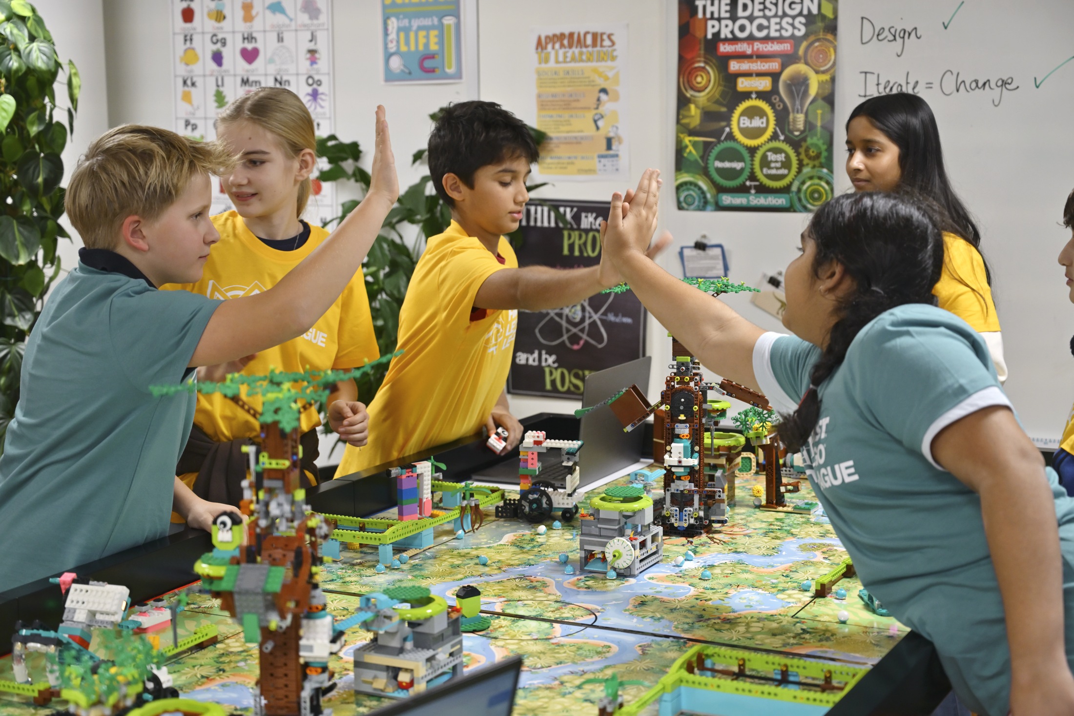 Alunos celebram em equipa junto de construções LEGO e do campo de desafios.